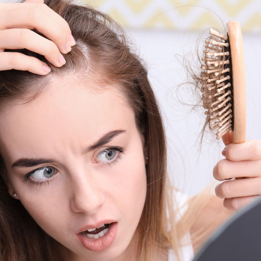 A woman who is losing her hair looks worriedly at the brush with her hair stuck to it.